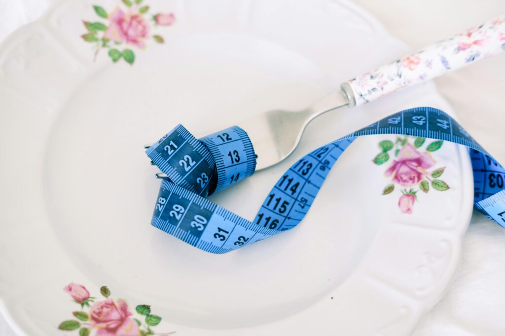 A floral plate with a fork and blue measuring tape symbolizing dieting or healthy eating.