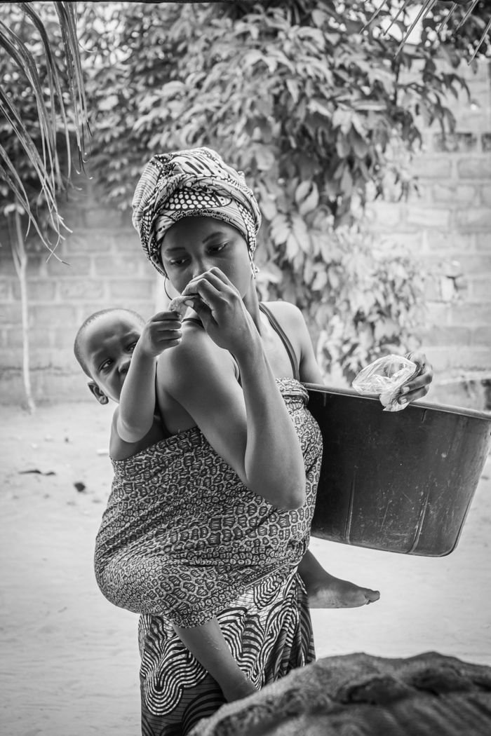 A black and white photo of a mother carrying her child in a traditional wrap outdoors.